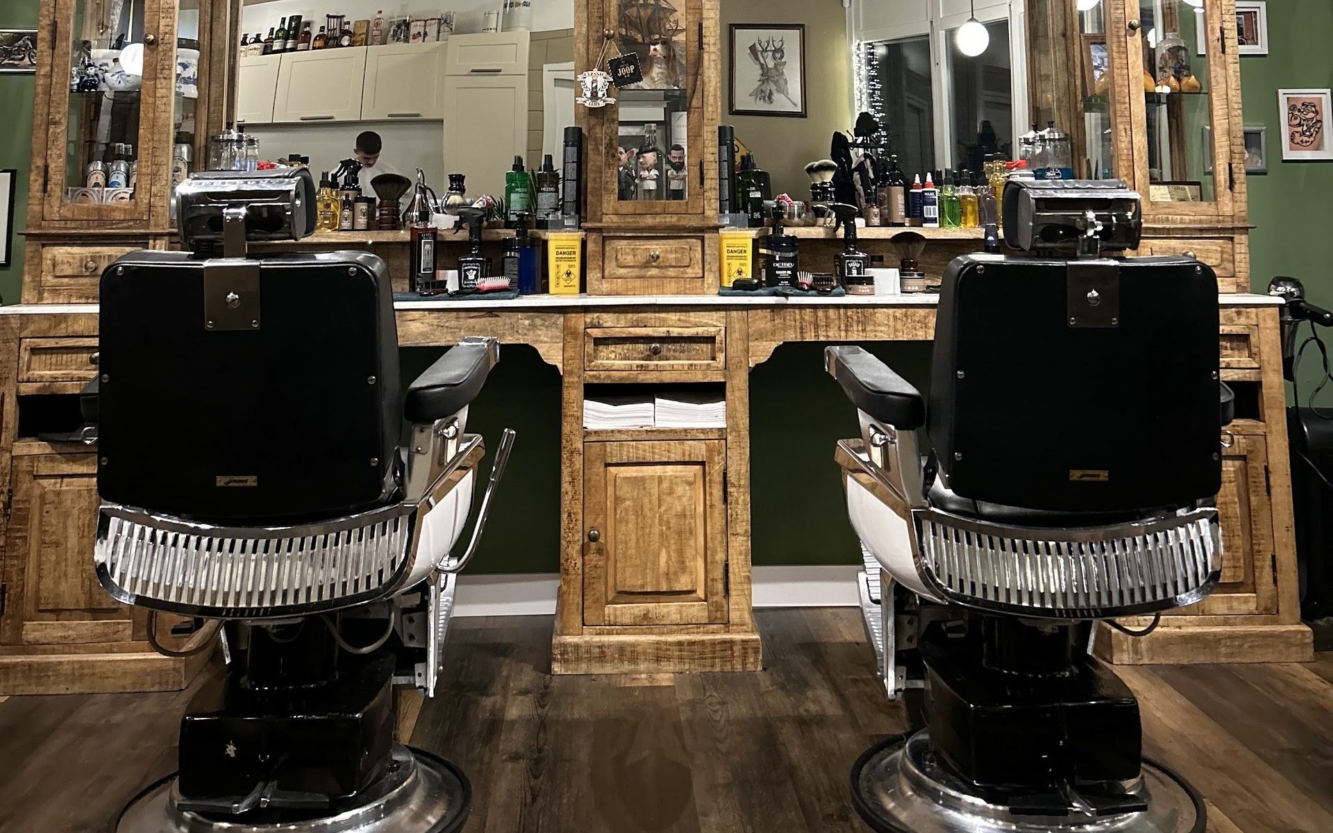 Twee zwarte barberstoelen voor het houten kappersmeubel met spiegels bij Classic Clips